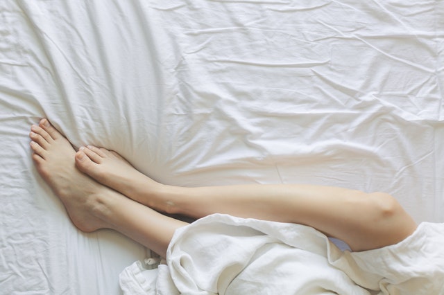 Ľudské nohy zakryté plachtou v posteli 